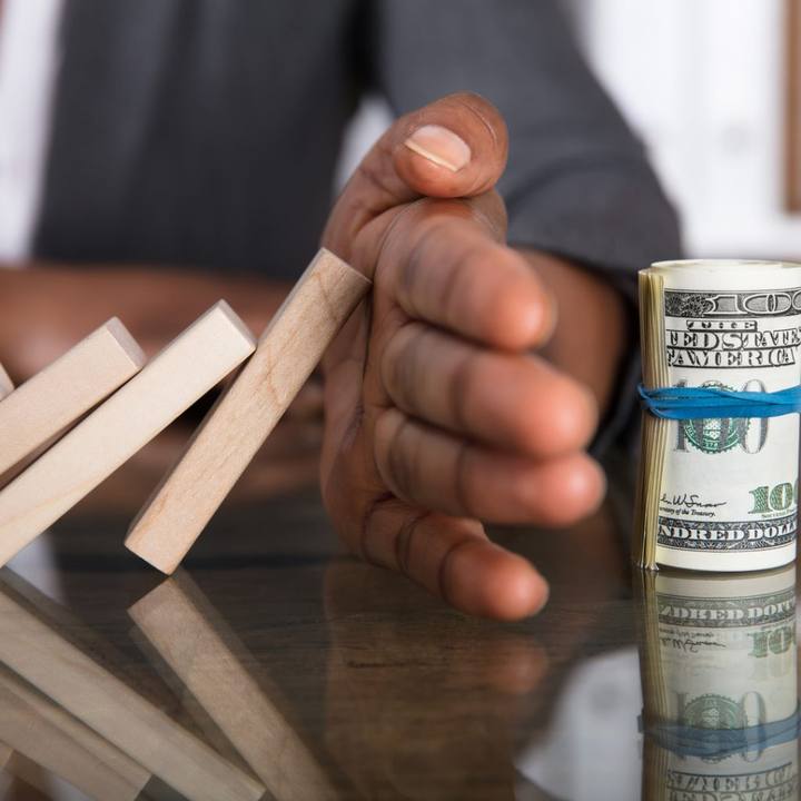 A hand stopping falling dominoes next to cash